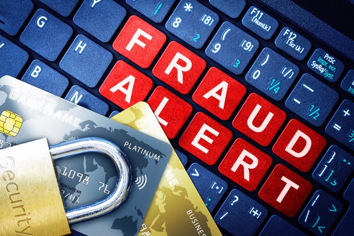 A dark blue computer keyboard with “Fraud Alert” on red tiles with silver and gold credit cards and a gold padlock on top.